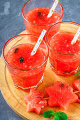 Watermelon smoothies in glasses with mint leaves on a gray dark concrete background.