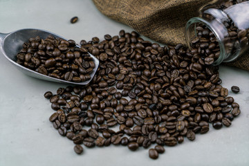 Close-up of roast coffee beans pilled out of a glass jar and scoop on the gray stone table on black background