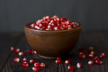 ruby pomegranate seeds in a clay bowl on wooden table