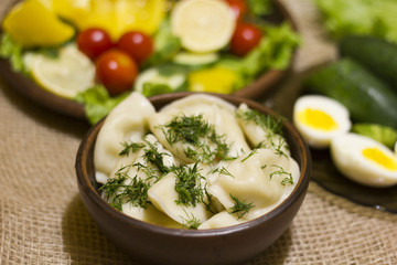 Closeup view of traditional russian food - pelmeni, ravioli or meat dumplings. Served with eggs, tomatoes, salad, marinated mushrooms, sauerkraut, cucumbers, green onion and garlic. Copy space