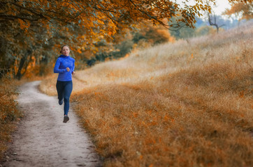 Fototapeta premium young slim athleic jogger woman runs along the path on the beautiful autumnal forest.