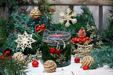 A jar with a candle, surrounded by Christmas decorations on the background of wooden boards.