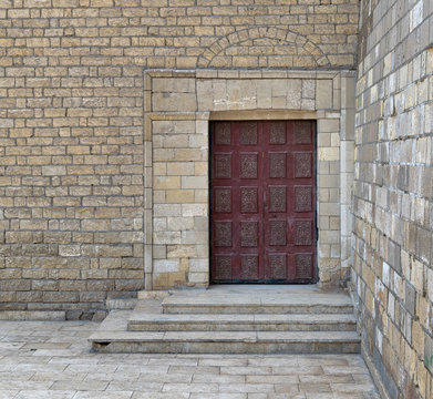 Wooden ornate engraved red door on bricks stone wall and deck stairs, exterior of Al Hakim Mosque (The Enlightened Mosque), Cairo, Egypt