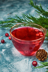 A fresh juicy drink made from cranberry berries in a glass cup on a blue marble background with spruce branches and cones with a copy of the space
