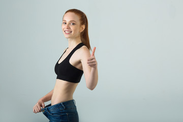 beautiful slender girl with red hair in sportswear on a light background demonstrates her slim figure