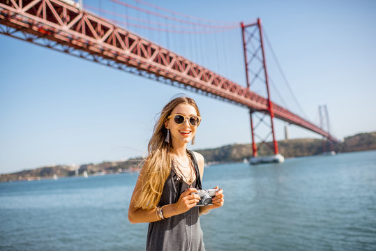 Portrait of a young woman tourist with photo camera standing in front of the famous iron bridge traveling in Lisbon city, Portugal