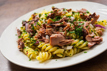 pasta fusilli salad with tuna and onion in white plate on a wooden background