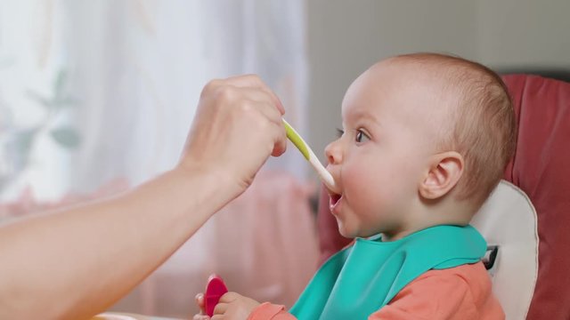 A baby girl eating puree at home. Medium shot. Soft focus.