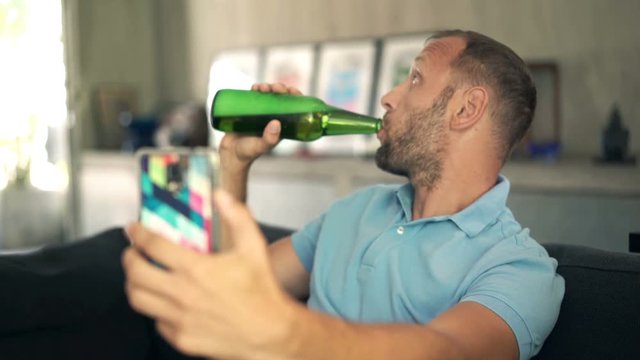 Young man with beer taking selfie photo with cellphone on sofa at home
