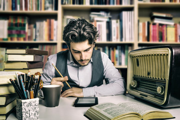 Young adult reading an ebook over a desk full of books and various objects