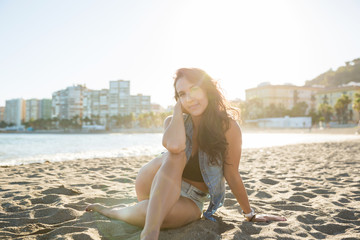 Young dreamy woman sitting on beach looking away