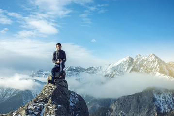 Young man in a sweater with phone in hand on the top of a snowy mountain. Concept availability of...