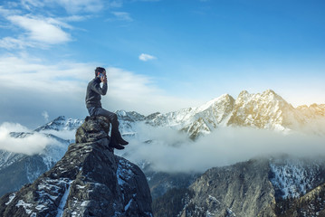 Young man in a sweater with phone in hand on the top of a snowy mountain. Concept availability of...