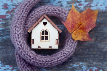  toy house is wrapped in a warm scarf with an autumn leaf.