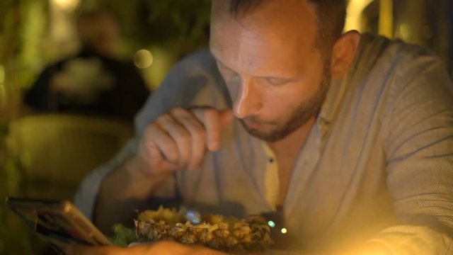 Man texting on smartphone and eating pineapple in cafe
