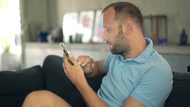 Happy, young man texting on smartphone on sofa at home
