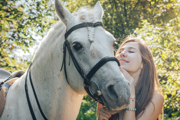 Girl teenager and white horse in a park in a summer