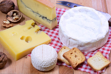 French cheese platter - Camembert, Morbier, Emmental and Goat cheese on red country style napkin and wooden board. Top view.