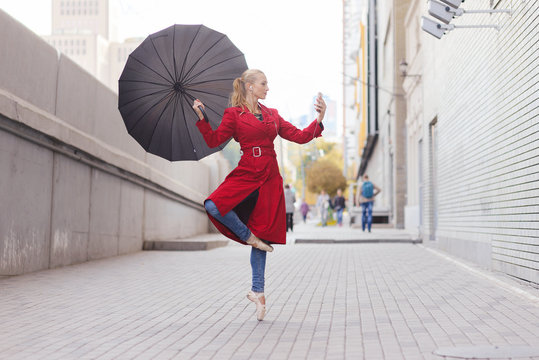 Woman ballerina dance with umbrella in city. Making selfie with smartphone