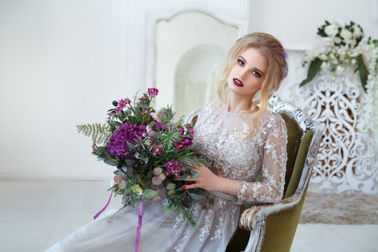 Portrait of a cute bride girl sitting in a chair with a bouquet in hands.