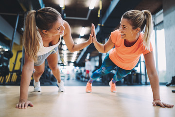 Two sporty girls doing push ups in gym - obrazy, fototapety, plakaty
