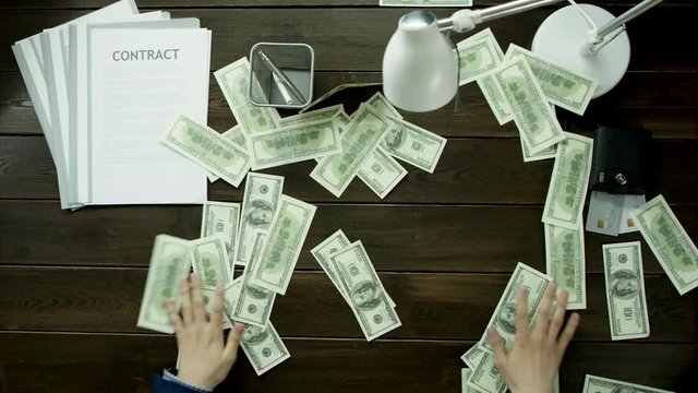 Money is scattered all over the office table and the man collects them.