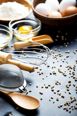 Baking ingredients. Bowl, eggs, flour, eggbeater, rolling pin and eggshells on black chalkboard from above.