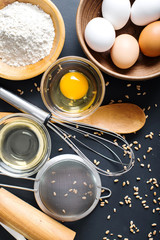 Baking ingredients. Bowl, eggs, flour, eggbeater, rolling pin and eggshells on black chalkboard from above.