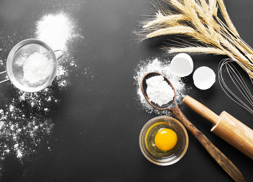 Baking ingredients. Bowl, eggs, flour, eggbeater, rolling pin and eggshells on black chalkboard 