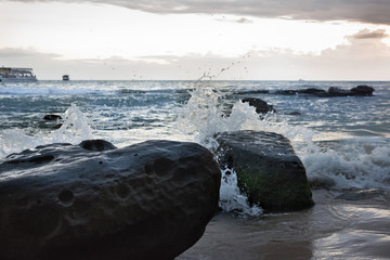 Sunset in Cambodia at the seaside. Sea waves roll on sands and rocks.
