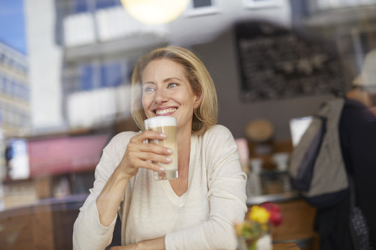Portrait of smiling woman drinking Latte Macchiato in a coffee shop