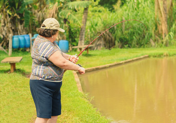 Old woman holding a fishing rod, hooking a fish on a lake. Brazilian women descendant of japanese fishing. 