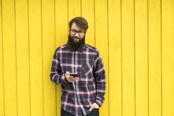 a young man with a smartphone in front of a yellow wall