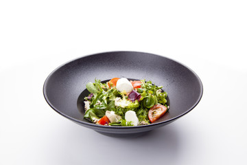 Italian mozzarella cheese and tomato salad with tomatoes and crisp crunchy fried bread cretins, view from above on a black  plate on white background.