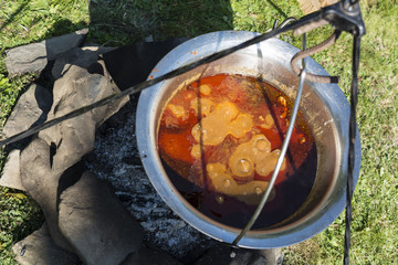 Pot goulash cooked over a fireplace on a tripod.