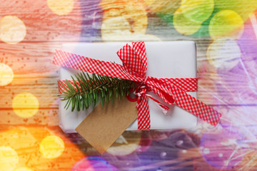 Holiday gift box. Christmas present with tag at white wooden table with bokeh effect