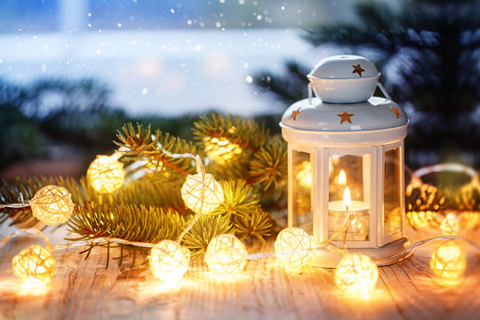 Christmas decoration with white candle lantern, fir tree branches and luminous garland.
