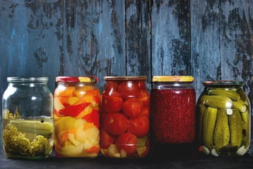 Photo sur Plexiglas Légumes Variety glass jars of homemade pickled or fermented vegetables and jams in row with old dark blue wooden plank background. Seasonal preserves.