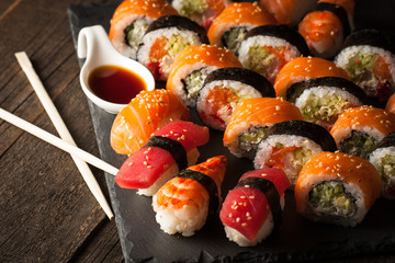 Sashimi and sushi rolls on a stone slatter. Sushi set with salmon, prawns, soy souce, wasabi and ginger. Traditional Japanese cuisine.