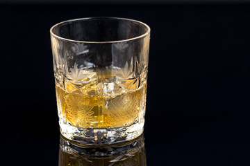 Glass of whiskey with ice cubes on the black background with reflections
