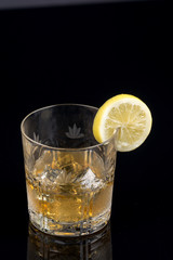 Glass with alcohol drink and lemon on the black background with reflections