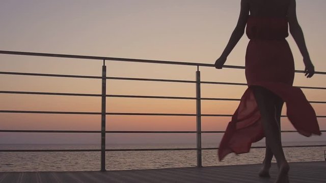 Young woman admires the sunset over the sea standing on the terrace