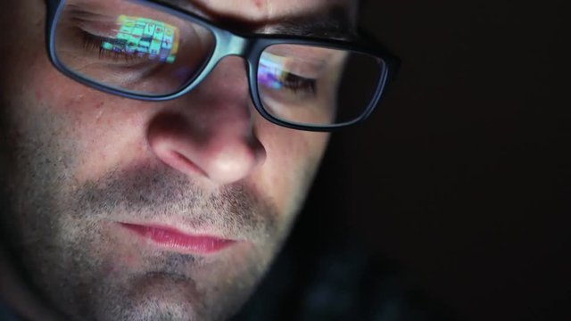 Gambling addicted man with glasses in front of online casino slot machine on laptop computer at night - loosing his money. Dramatic low light grain shot.