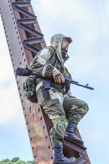 Soldier in uniform with a hood on his head on a railway bridge with an automatic weapon