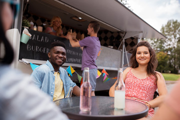 friends with drinks sitting at table at food truck