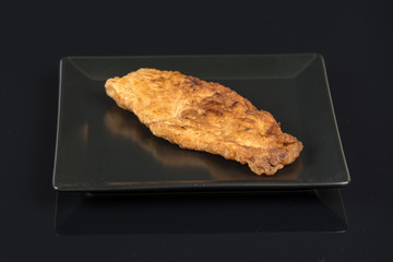 Fried breaded chicken white meat on the black square plate above black background