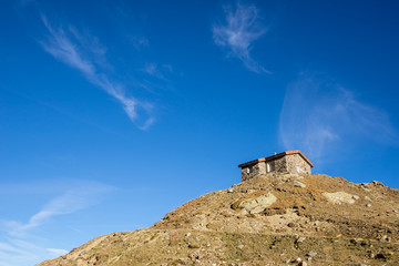 Fototapeta premium Timmelsjoch High Alpine Road, house on the hill landscape. Mountains and peaks natural environment. Hiking in the Passo del Rombo. Ötztal alps, Austria and Italy border, Europe