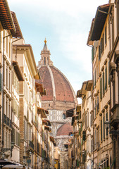 Florence street with old buildings and Santa Maria del Fiore dome on horizon.