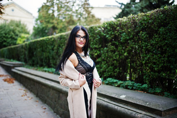 Black hair sexy woman in glasses and coat posed on street.