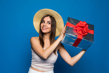 Portrait of a smiling pretty girl holding gift box isolated over blue background. Woman listen what inside of box.